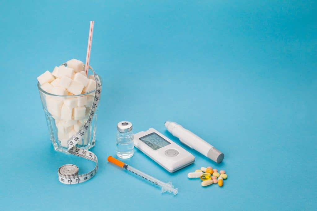 Diabetes, medical concept of blood sugar, insulin syringes and pills with measuring tape and a glass full of cubic meters of sugar