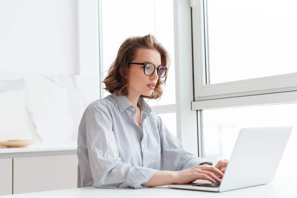 Photo of young concentrated woman in striped shirt using laptop